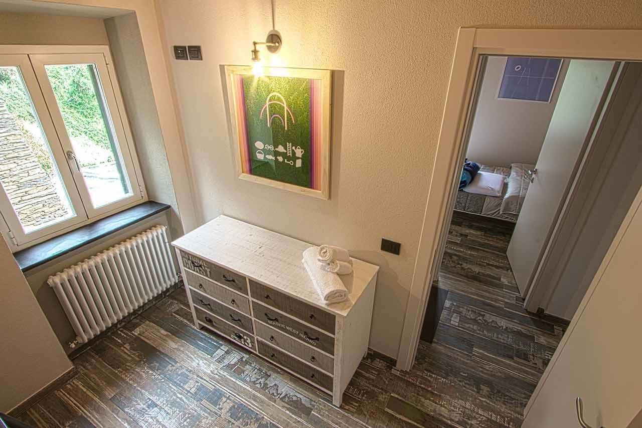 A bathroom with a wooden floor, a white cabinet with drawers, a towel on top, and a framed picture on the wall.
