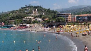 A beach with clear blue water, umbrellas, and people. - Oltremare Guest House (Lavagna)