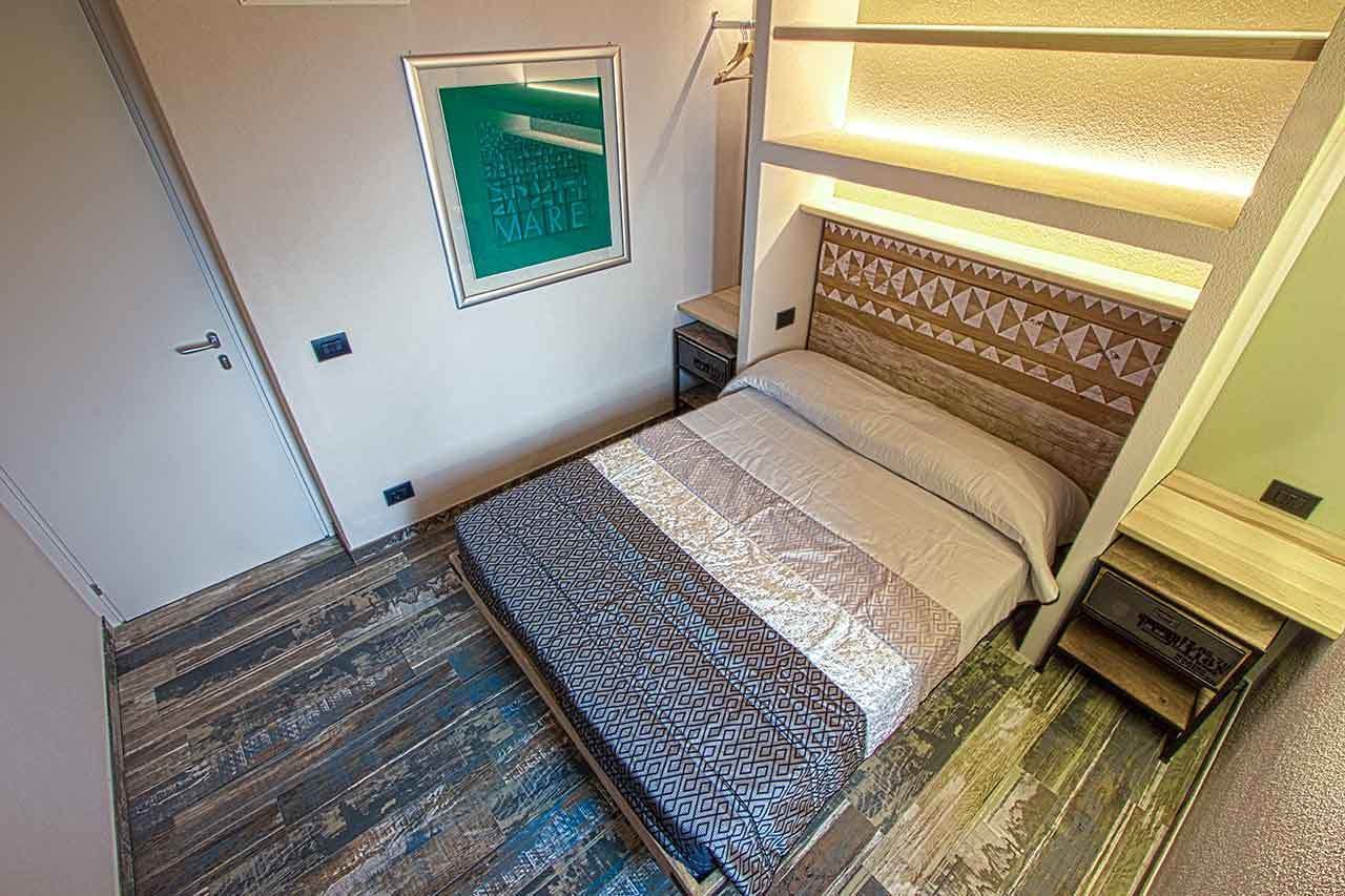 Una habitación compacta con una cama, una mesita de noche pequeña, un estante en la pared y un cuadro enmarcado.