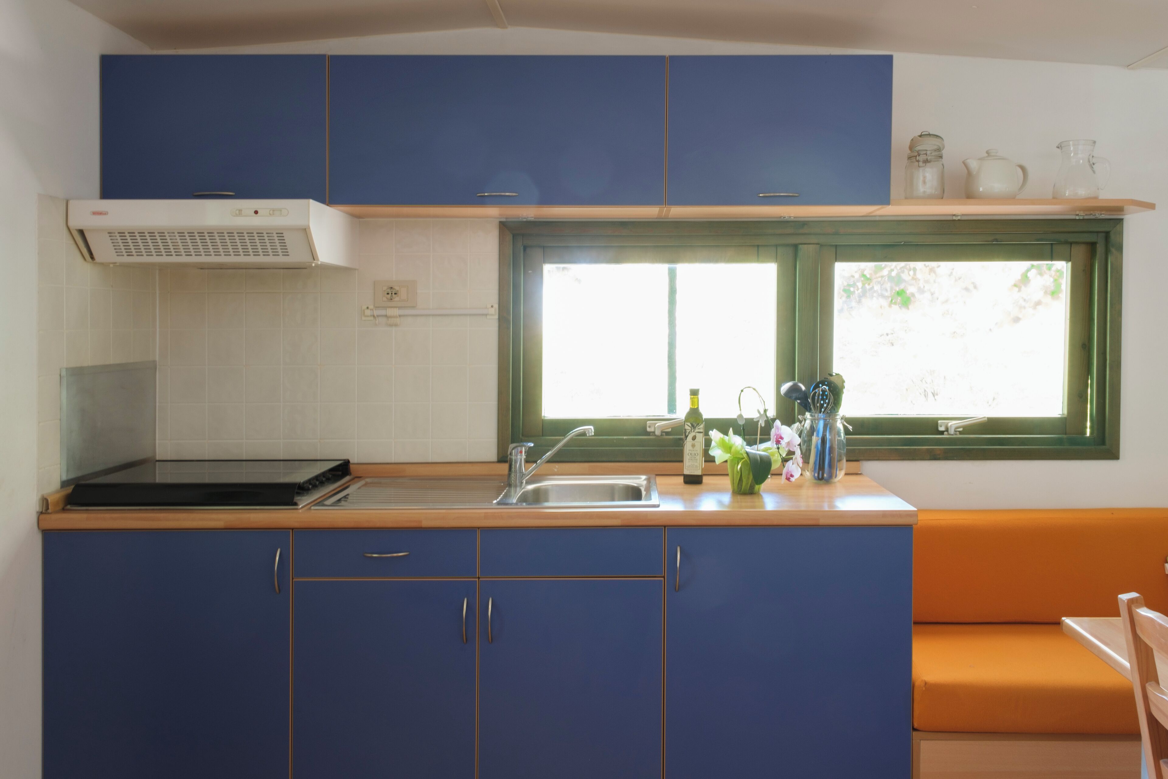 Cocina compacta con armarios azules, encimera de madera, estufa integrada y ventana con vistas al verdor.
