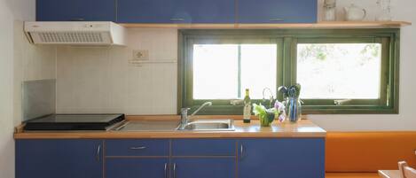 Cocina compacta con armarios azules, encimera de madera, estufa integrada y ventana con vistas al verdor.