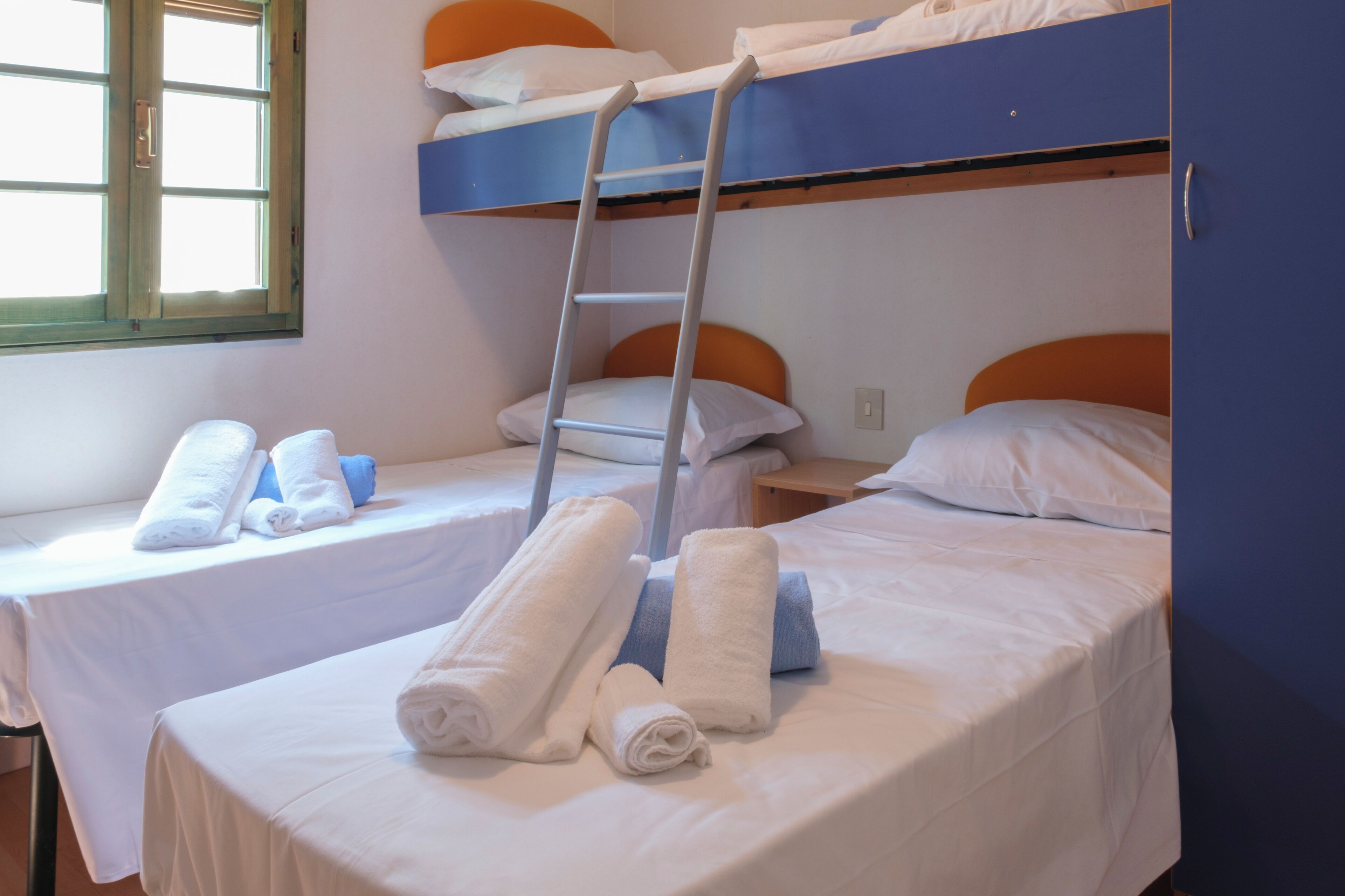 A dormitory room with bunk beds, a ladder, and neatly folded towels on each bed.