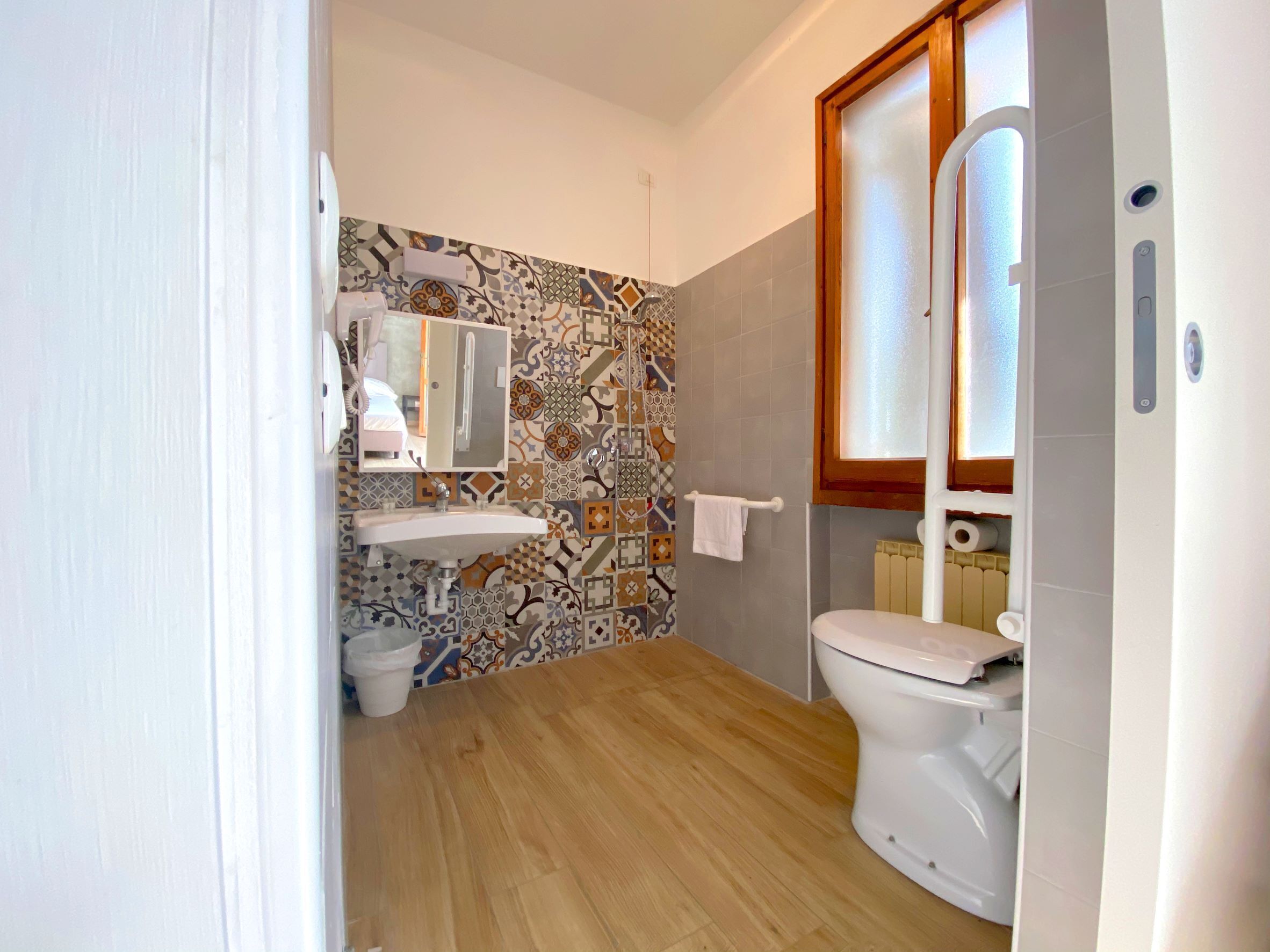 A bathroom with a tiled wall, a sink, a toilet, and a window.