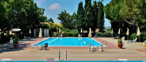 A rectangular swimming pool with a tiled deck, surrounded by trees and outdoor seating.