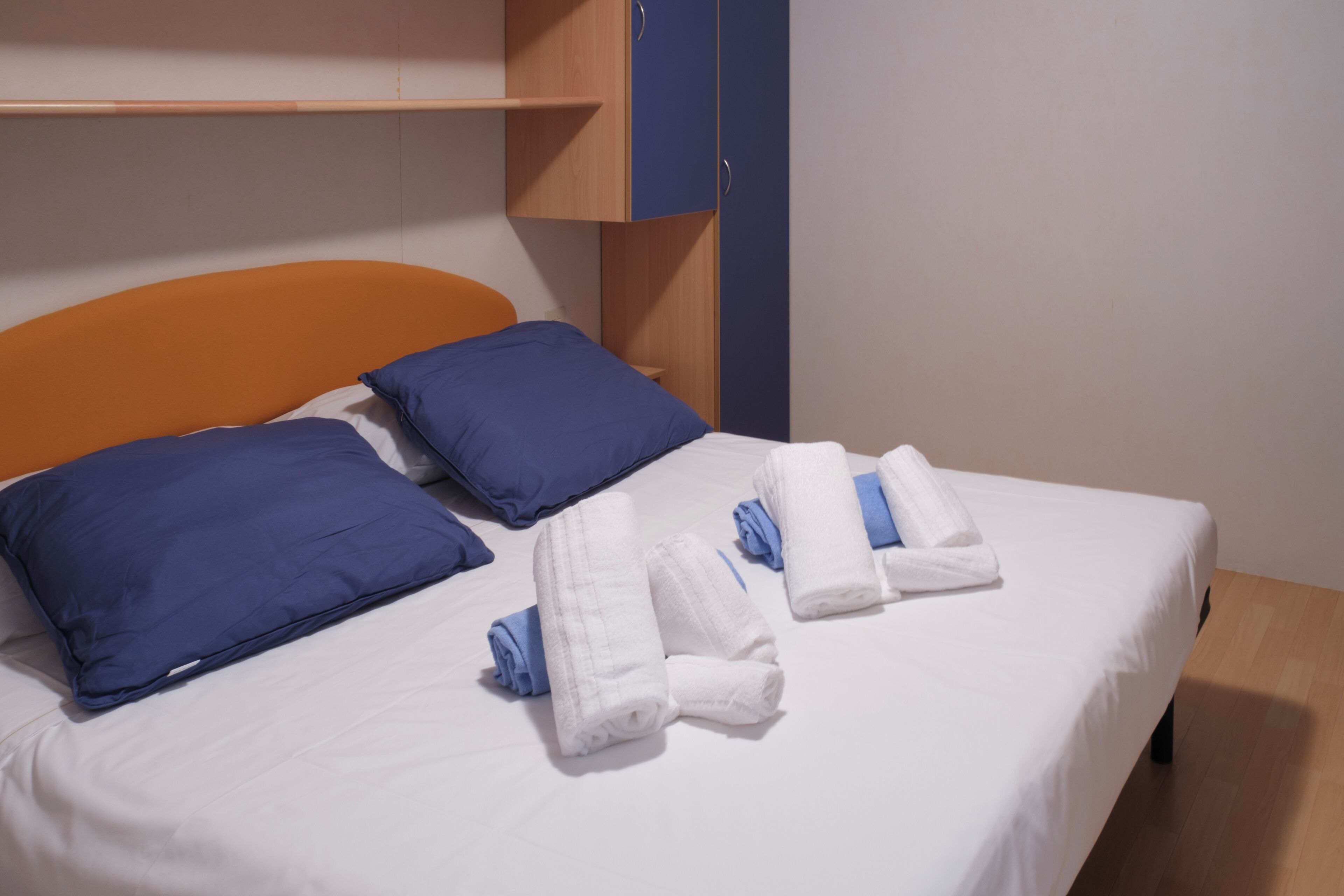 Un lit bien fait, avec des oreillers et des serviettes bleues et blanches, une tête de lit en bois et une armoire en bois.