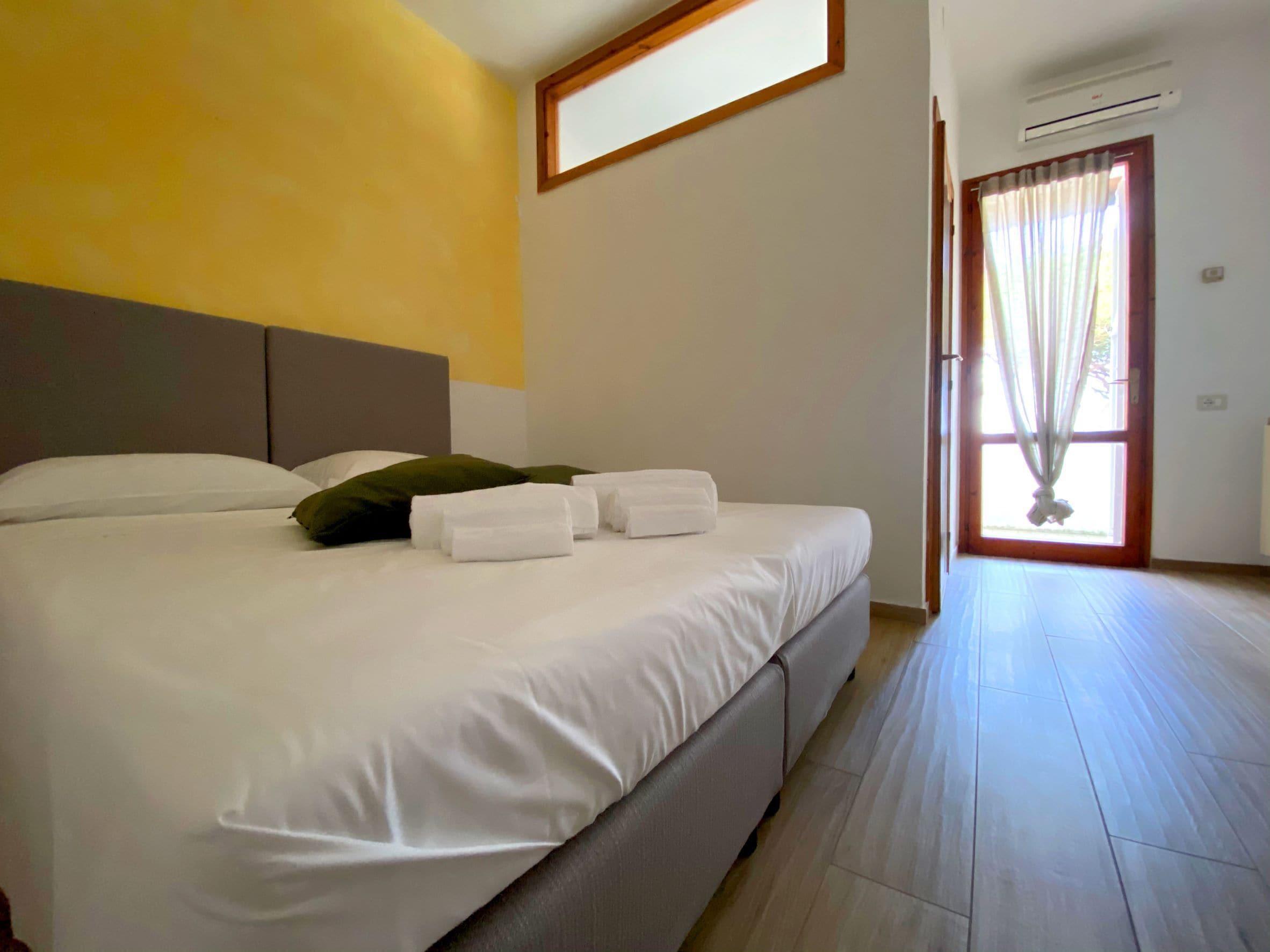 A bedroom with a large bed, a window with curtains, and an air conditioning unit.