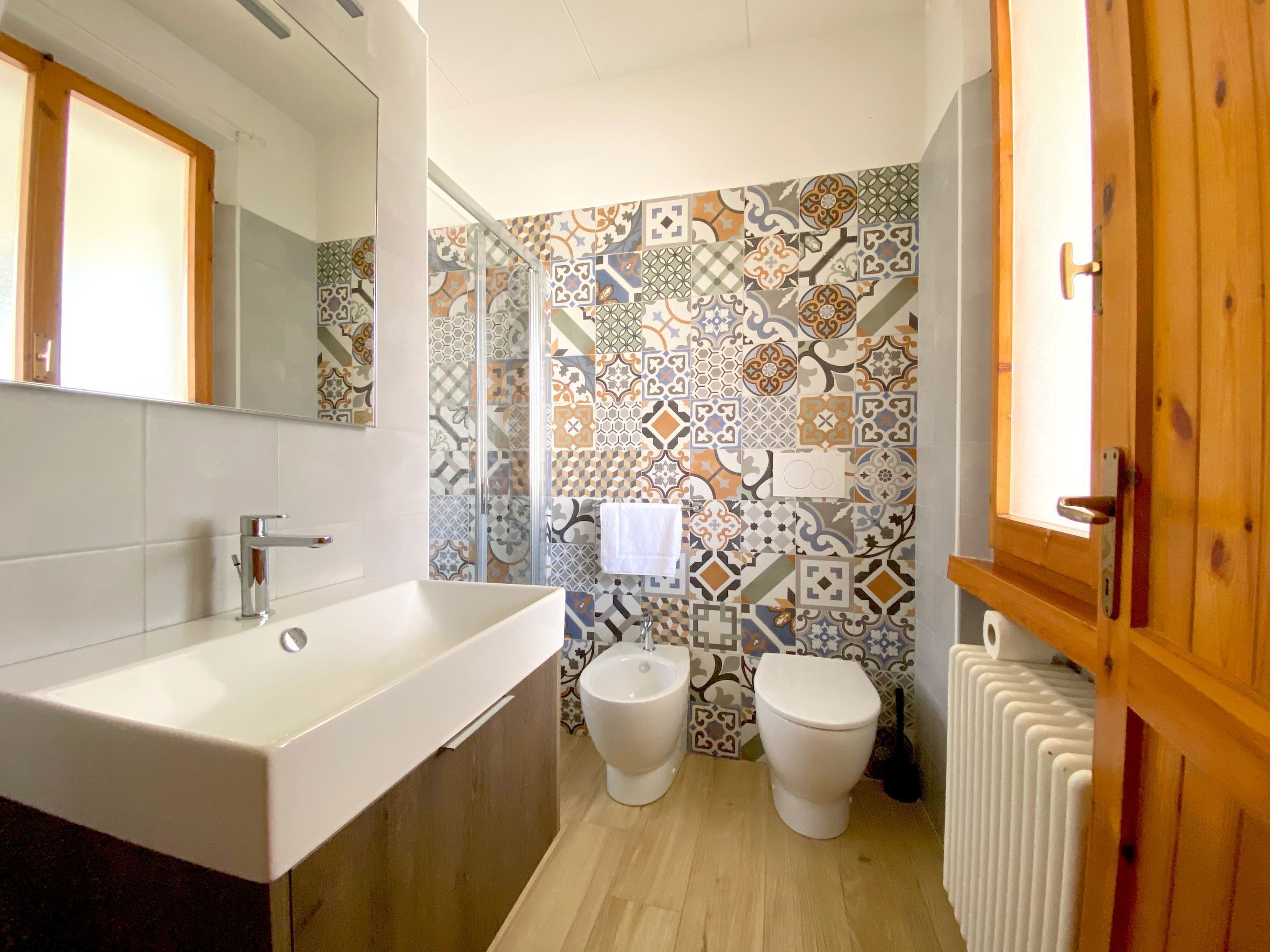 A bathroom with a white sink, two toilets, a shower, and a radiator.