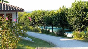 Propiedad campestre con camino de grava, un edificio blanco de techo a dos aguas y abundante vegetación.