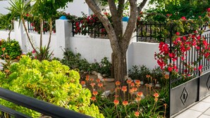 Un balcón con vistas a un jardín, que incluye un árbol, diversas plantas y una barandilla de metal.