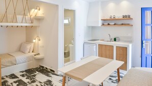 Un dormitorio pequeño con cama, mesita de noche y un escritorio. Junto a él, una kitchenette con lavabo, estufa y armarios de almacenamiento.