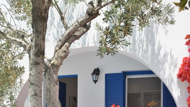 Un edificio blanco con contraventanas azules y un balcón adornado con flores rojas.