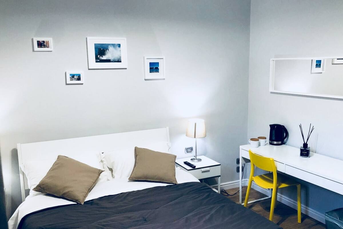 A hotel room with a bed, bedside table, lamp, desk, chair, and wall-mounted pictures.