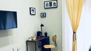 A small, modern room with a wooden floor, a desk with a chair, a TV mounted on the wall, and a bed. - Palazzo Ferrara (Naples)