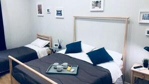 A hotel room with two beds, a bedside table with a tray of tea and a remote control, and framed pictures on the wall. - Palazzo Ferrara (Naples)