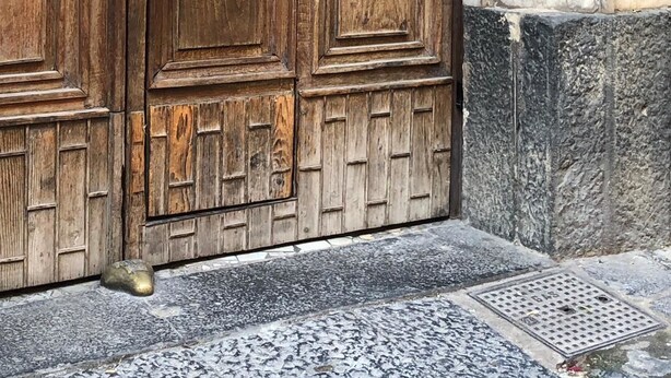 A wooden door with a metal handle, a stone wall, and a metal vent. - Palazzo Ferrara (Naples)