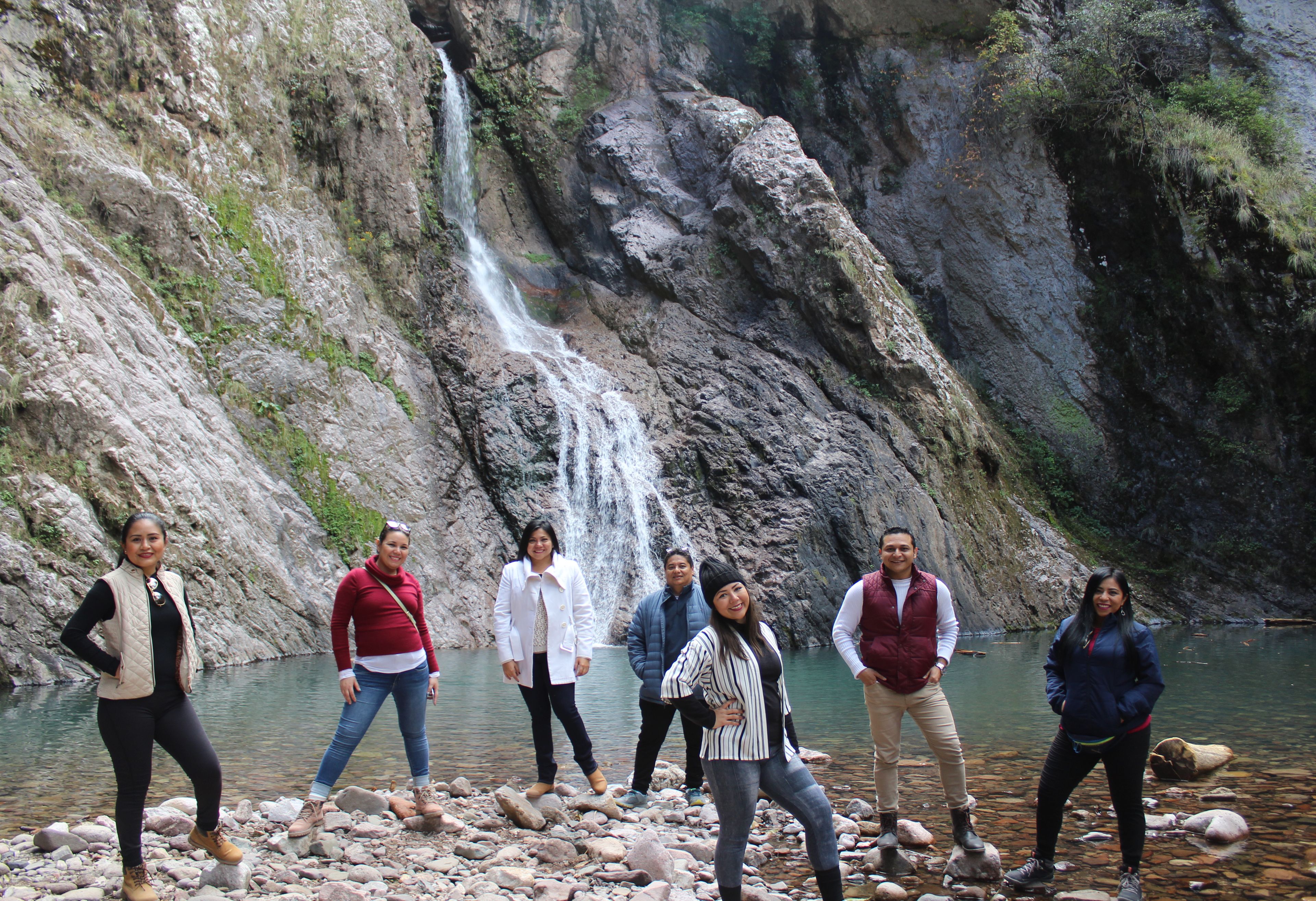 A group of people standing on rocks by a waterfall.