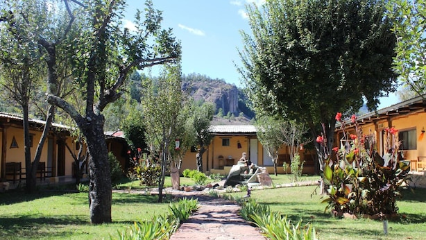A courtyard with a stone pathway leading to a building with a tiled roof. - Hotel Paraiso del Oso (Urique)
