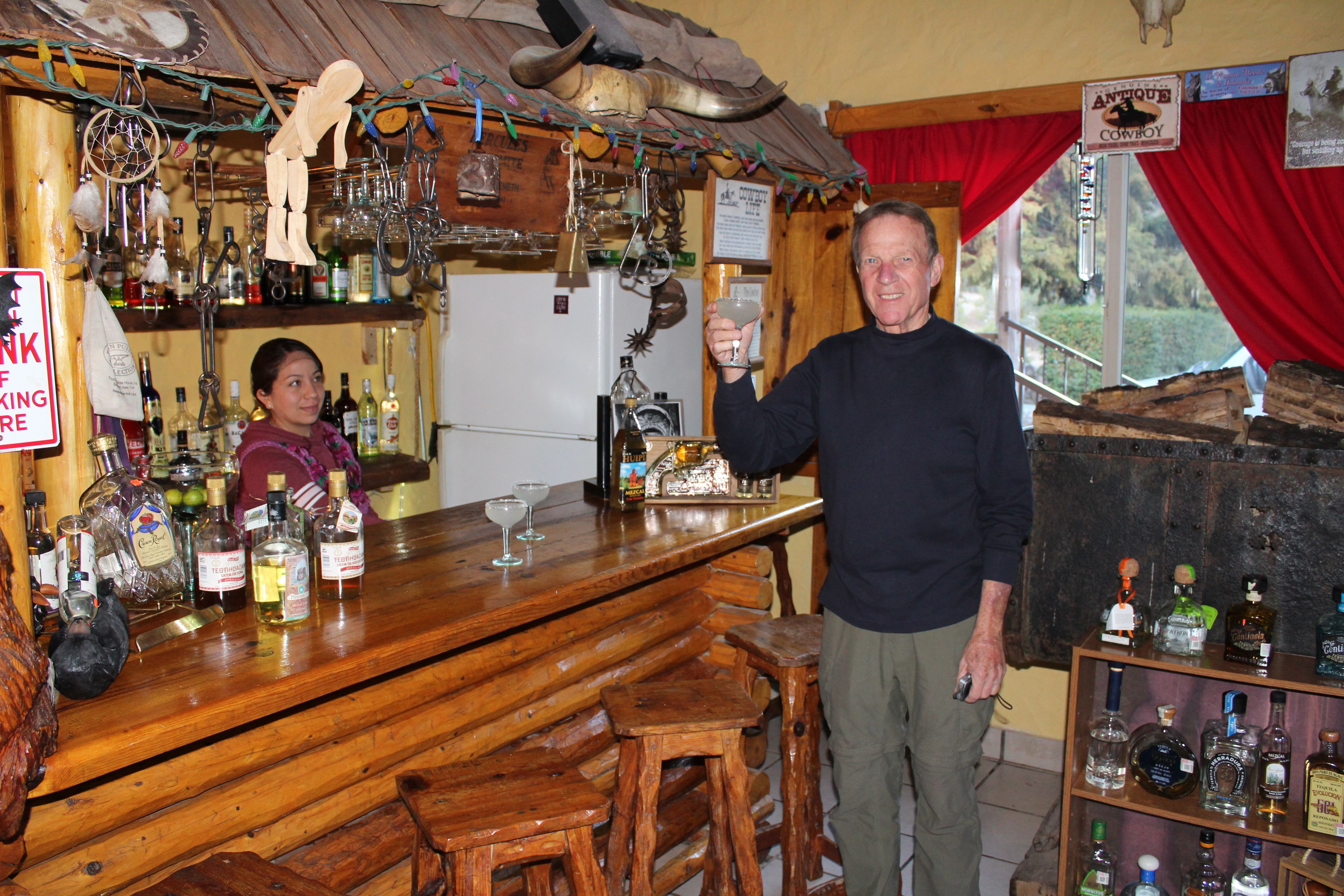 A bar area with wooden furniture, shelves with bottles, and a rustic decor including a cow skull and antler.