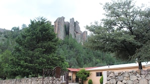 A stone-walled building with a red roof, surrounded by greenery and a rocky mountain backdrop. - Hotel Paraiso del Oso (Urique)