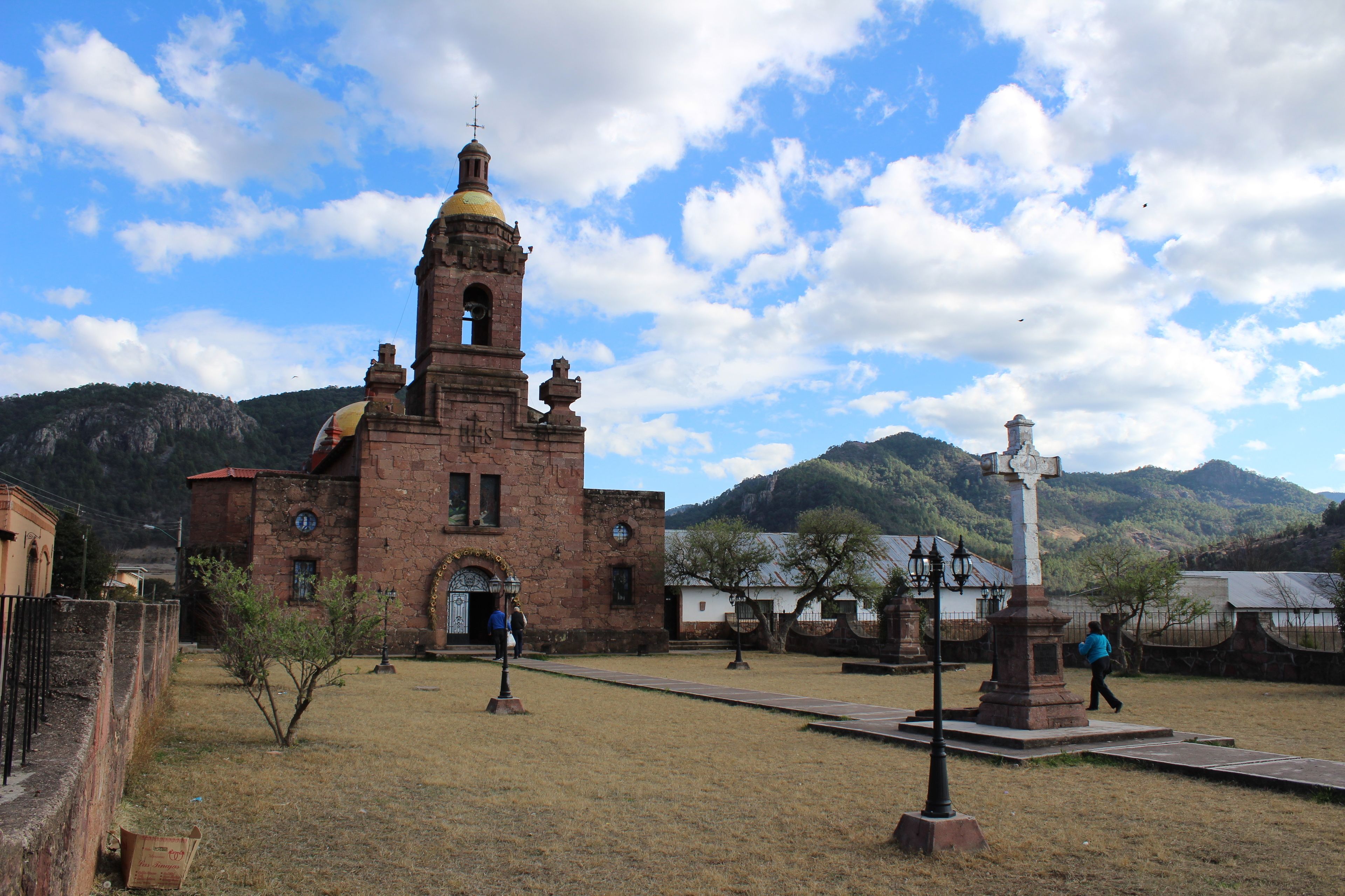 A historic church with a bell tower and a cross monument in a rural setting.