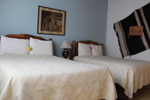 Habitación de hotel con dos camas, un cuadro enmarcado en la pared, una lámpara y una manta a rayas blanco y negro colgada en la pared.
