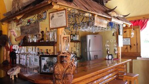 A rustic bar area with wooden furniture, a large wooden sculpture, and various bottles and glasses. - Hotel Paraiso del Oso (Urique)