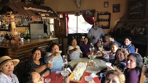 A group of people seated around a table with drinks, in a rustic setting with wooden furniture and a bar area in the background. - Hotel Paraiso del Oso (Urique)