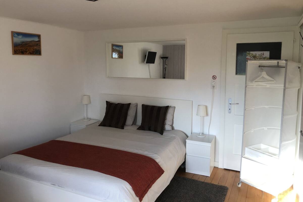 Un dormitorio con cama, mesitas de noche, un espejo, perchero y una puerta.