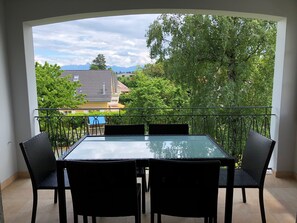 A balcony with a glass table and four chairs, offering a view of a mountain range and trees. - Au Bonheur des Iris (Rolle)