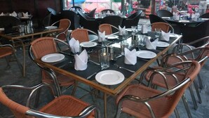 A restaurant with tables set for dining, wicker chairs, and a view of an amusement park in the background. - GreyVillas (Murree)