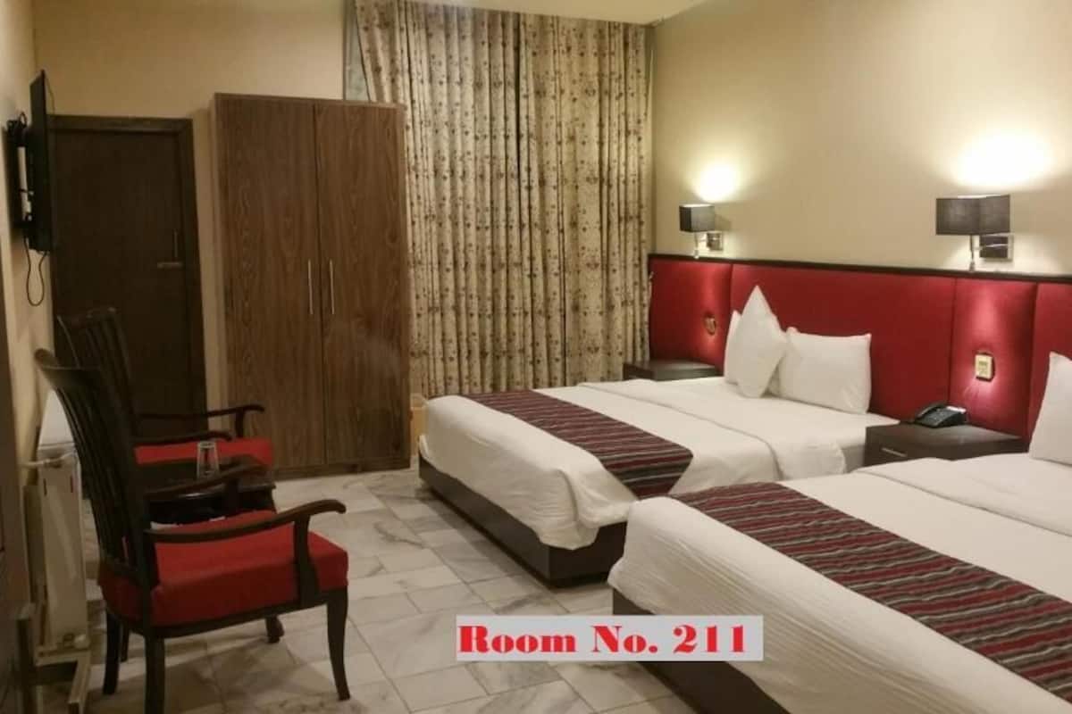 Habitación de hotel con dos camas, una silla, un armario y una cortina.