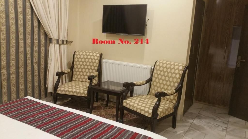 Une pièce comprenant deux fauteuils à motifs, une petite table, un téléviseur fixé au mur et un tapis à rayures.