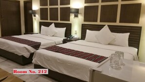 A hotel room with two beds, a nightstand, a bedside table with glasses, and a wall-mounted lamp. - GreyVillas (Murree)