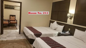 A hotel room with two beds, a nightstand, a lamp, and a chair. - GreyVillas (Murree)