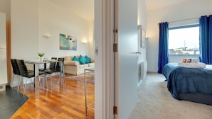 A modern hotel room with a dining area, a bed with a view, and a small table with chairs. - Crown Apartments By Week2Week (Newcastle-upon-Tyne)