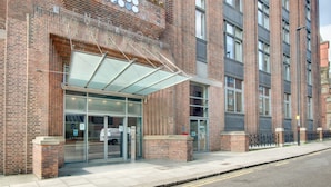 A modern building with a glass entrance, brick facade, and a covered waiting area. - Crown Apartments By Week2Week (Newcastle-upon-Tyne)