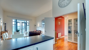 A modern kitchen with a black countertop, white cabinets, and a large window. - Crown Apartments By Week2Week (Newcastle-upon-Tyne)