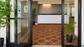 A hotel entrance with a glass door, a patterned carpet, and potted plants. - Morton Inn (Morton)