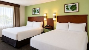 A hotel room with two beds, a wooden headboard, bedside lamps, a telephone, and framed leaf artwork on the wall. - Morton Inn (Morton)