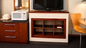 A hotel room with a television, microwave, wooden cabinet, and a small table with a chair. - Morton Inn (Morton)