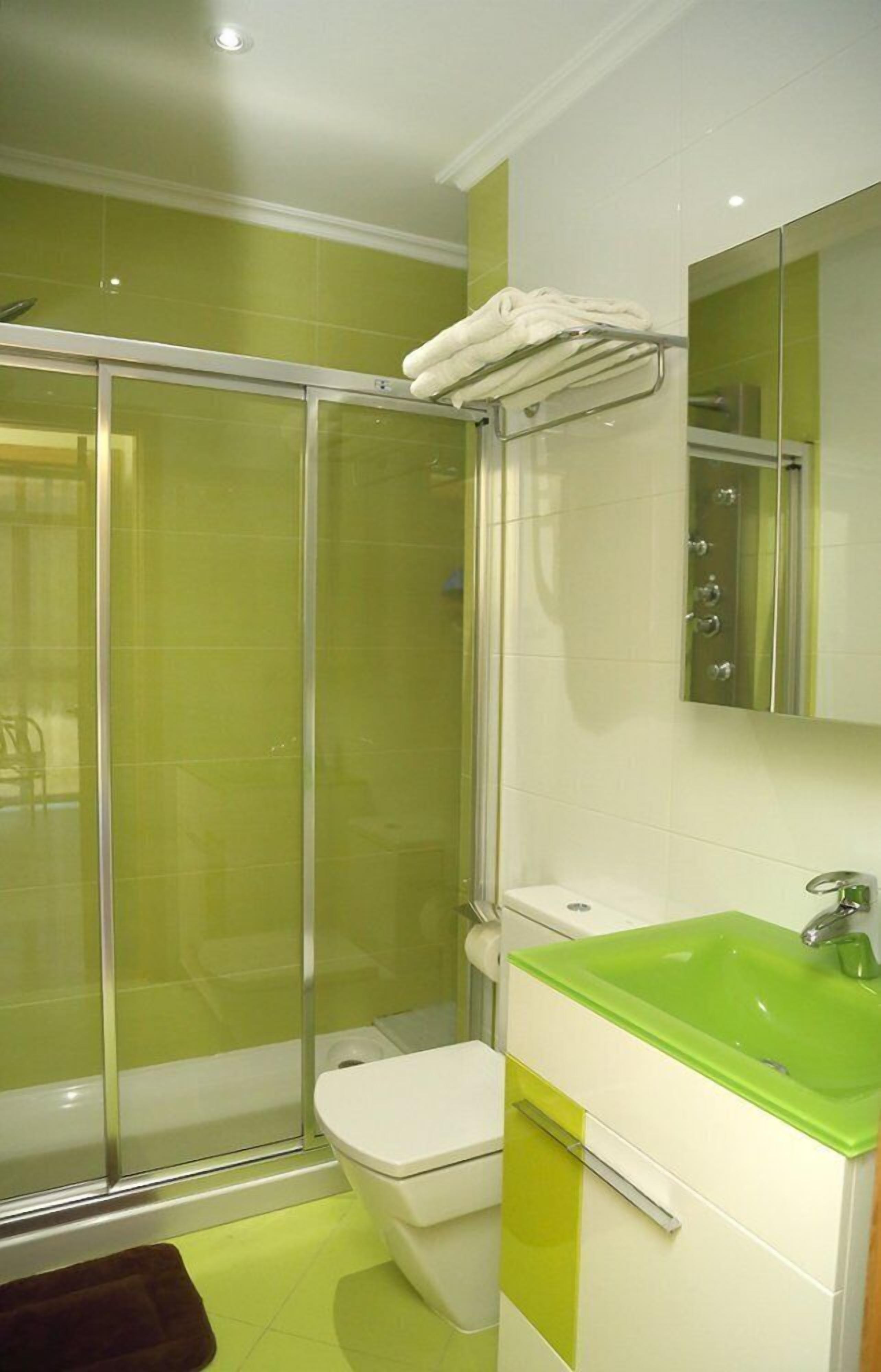 Un baño con cabina de ducha de vidrio, inodoro blanco y lavamanos verde.