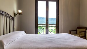 A hotel room with a large bed, a chair, and a balcony with a view of the mountains. - Apartamentos Rurales Abelleira (Muros)