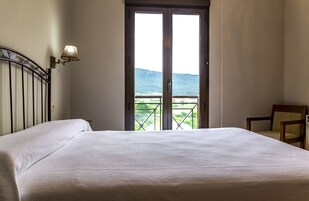 Habitación de hotel con cama grande, una silla y balcón con vistas a las montañas.