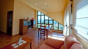 A spacious living area with a dining table, sofa, and a television. - Apartamentos Rurales Abelleira (Muros)