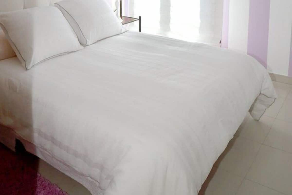 Un dormitorio con una cama grande, una mesita de noche y un ventanal con cortinas.