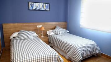 Una habitación con dos camas, cada una con una colcha a cuadros, una mesita de noche con una lámpara y un cuadro en la pared.