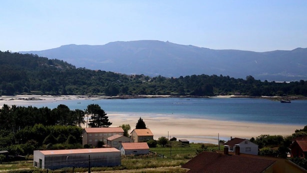 A coastal area with buildings near a beach and mountains in the background. - Apartamentos Rurales Abelleira (Muros)