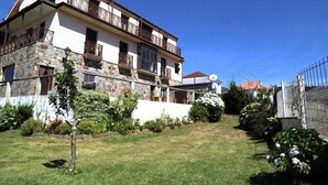 A two-story building with a stone facade, balconies, and a well-maintained garden. - Apartamentos Rurales Abelleira (Muros)