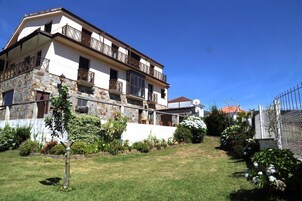 Un edificio de dos plantas con fachada de piedra, balcones y un jardín bien cuidado.