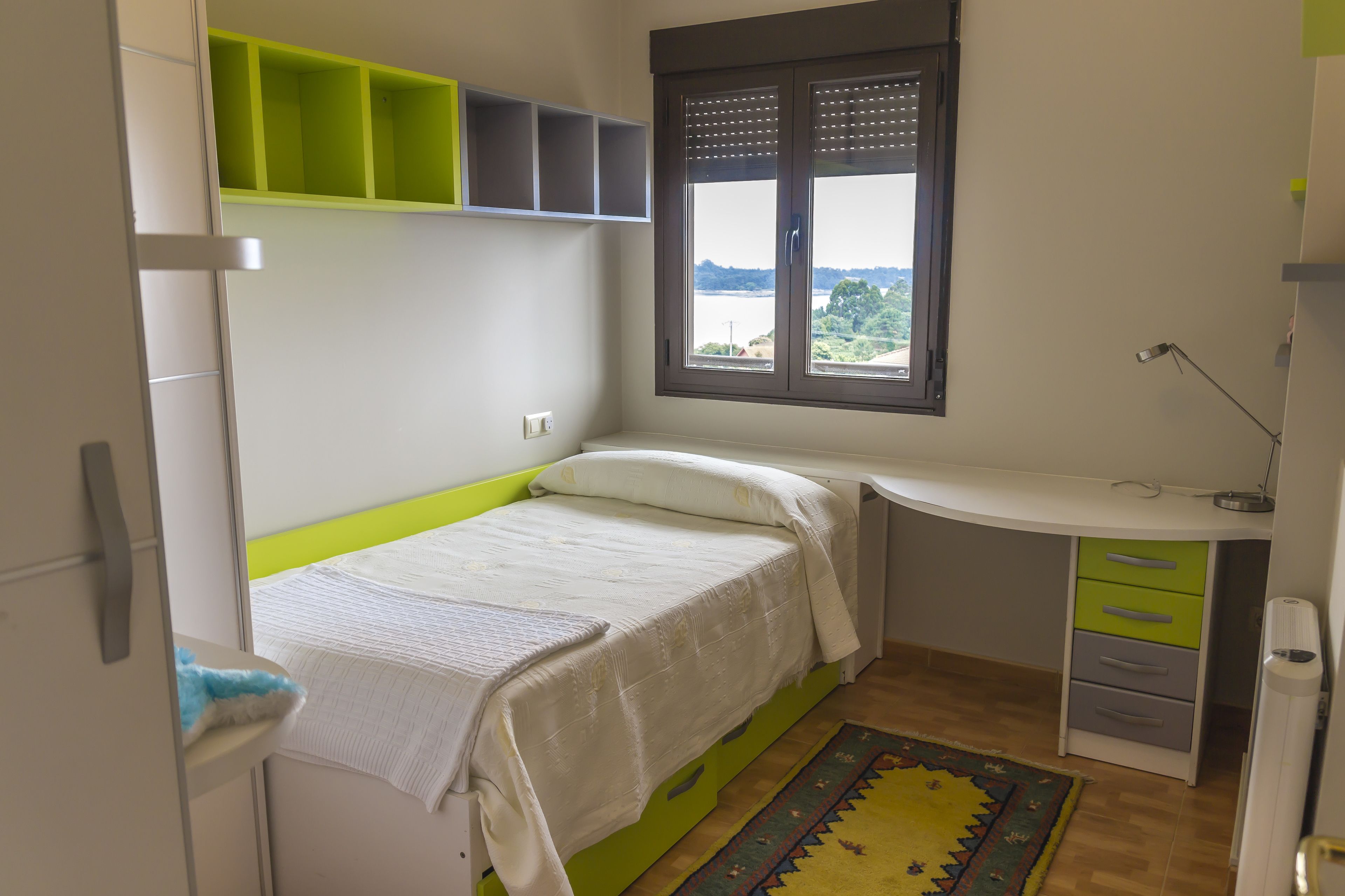 Een slaapkamer met een bed, een bureau en een raam met uitzicht.